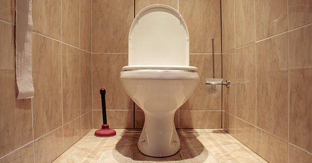 Toilet in a tiled bathroom with a plunger beside it, representing toilet installation and repair services by The Plumbing Dr in Arlington, VA.